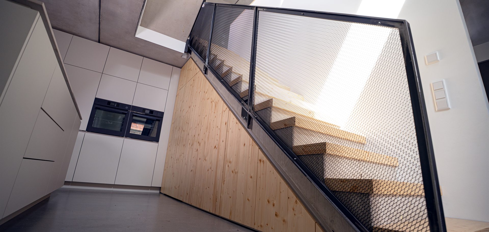 Sonnenlicht fällt durch Streckmetall-Geländer auf Holzstufen – Materialdetail Treppenbau Essen
